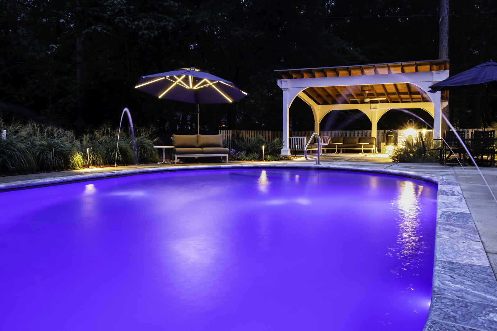 Backyard pool and covered pergola lit up in the evening